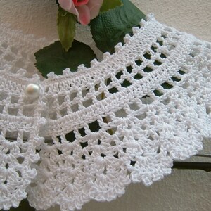 May include: White crocheted collar with a pearl button in the center.