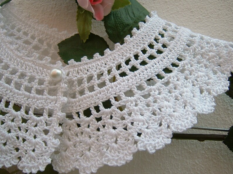 May include: White crocheted collar with a pearl button in the center.