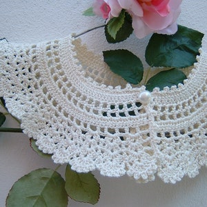 May include: A white crocheted collar with a pearl button in the center.