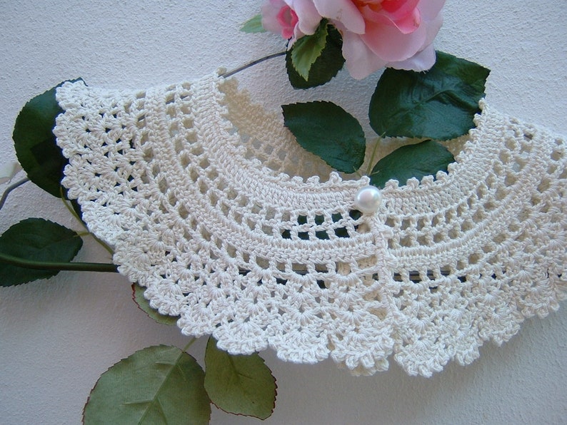 May include: A white crocheted collar with a pearl button in the center.