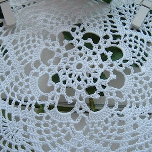 Peut inclure: Gros plan sur des napperons blancs faits &agrave; la main au crochet. Les napperons pr&eacute;sentent un motif ajour&eacute; d&eacute;licat avec un motif floral central. Les motifs complexes sont visibles, mettant en valeur le savoir-faire. Les napperons sont maintenus en place avec des pinces &agrave; linge blanches.