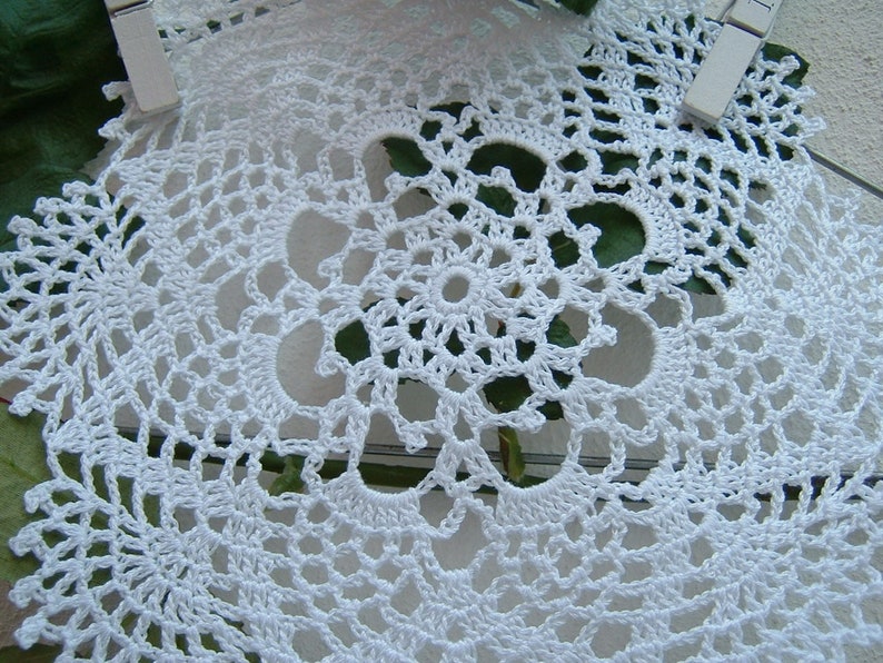 Peut inclure: Gros plan sur des napperons blancs faits &agrave; la main au crochet. Les napperons pr&eacute;sentent un motif ajour&eacute; d&eacute;licat avec un motif floral central. Les motifs complexes sont visibles, mettant en valeur le savoir-faire. Les napperons sont maintenus en place avec des pinces &agrave; linge blanches.