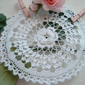 Puede incluir: Doily de ganchillo blanco con un delicado dise&ntilde;o floral. El doily es circular y tiene un centro con un patr&oacute;n de flor en relieve.