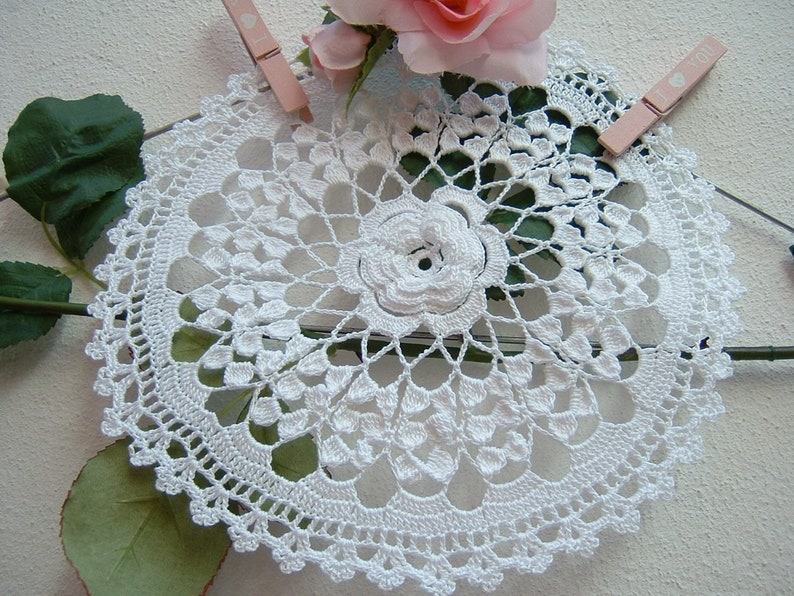 Puede incluir: Doily de ganchillo blanco con un delicado dise&ntilde;o floral. El doily es circular y tiene un centro con un patr&oacute;n de flor en relieve.