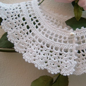 May include: White crocheted collar with a pearl button in the center.