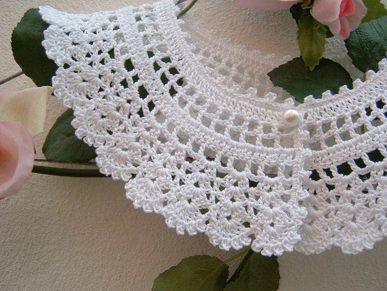 May include: White crocheted collar with a pearl button in the center.