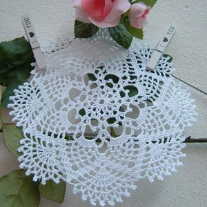 Peut inclure: Nappe blanche en crochet avec un motif floral d&eacute;taill&eacute;. La nappe est maintenue par deux pinces &agrave; linge, chacune avec le texte "I ❤ YOU". Une rose rose et des feuilles vertes sont en arri&egrave;re-plan.