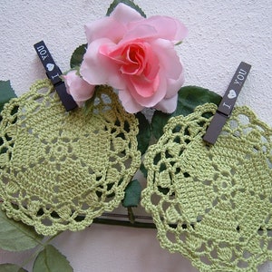 Puede incluir: Dos doilies de ganchillo verde con un delicado patrón de encaje. Cada doily está sujeto por una pinza de madera con las palabras "Te amo" impresas en ellas. Una rosa rosa es visible en el fondo.