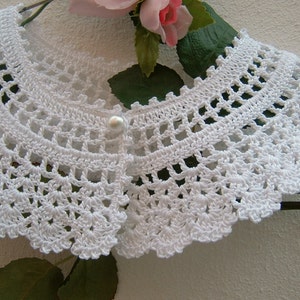 May include: White crocheted collar with a pearl button in the center.