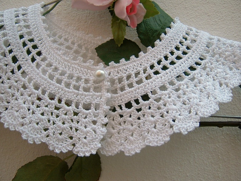May include: White crocheted collar with a pearl button in the center.