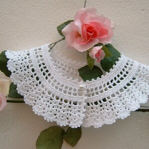 May include: White crocheted collar with a pearl button closure. The collar is on a hanger with pink roses and green leaves.