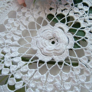 Puede incluir: Doily de ganchillo blanco con un delicado dise&ntilde;o floral. El doily presenta una gran flor en relieve en el centro, rodeada de motivos florales m&aacute;s peque&ntilde;os e intrincados.
