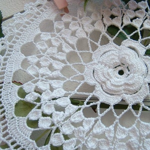 Puede incluir: Doily de ganchillo blanco con una gran flor en el centro. El doily tiene un delicado patr&oacute;n de encaje y es perfecto para agregar un toque de elegancia a cualquier hogar.