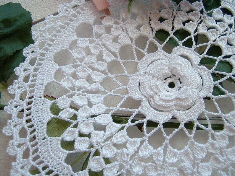 Puede incluir: Doily de ganchillo blanco con una gran flor en el centro. El doily tiene un delicado patr&oacute;n de encaje y es perfecto para agregar un toque de elegancia a cualquier hogar.