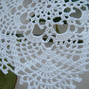 Peut inclure: Gros plan sur un napperon blanc crochet&eacute;. Le motif de dentelle complexe pr&eacute;sente un motif floral r&eacute;p&eacute;titif avec des d&eacute;tails ajour&eacute;s. Le napperon est fait d'un fil blanc doux et est probablement fait &agrave; la main. L'arri&egrave;re-plan est flou.