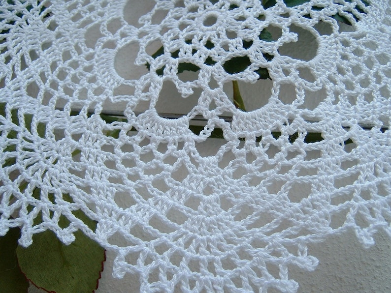 Peut inclure: Gros plan sur un napperon blanc crochet&eacute;. Le motif de dentelle complexe pr&eacute;sente un motif floral r&eacute;p&eacute;titif avec des d&eacute;tails ajour&eacute;s. Le napperon est fait d'un fil blanc doux et est probablement fait &agrave; la main. L'arri&egrave;re-plan est flou.