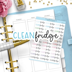 Può includere: Un foglio di adesivi per agenda con il testo CLEAN fridge in vari colori e caratteri. Gli adesivi sono disposti in file su un supporto azzurro, posizionati sopra un'agenda aperta con anelli dorati e una penna con motivo a griglia bianca.