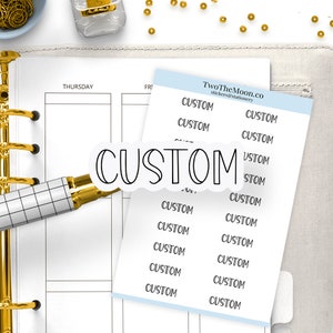 Può includere: Un foglio di carta bianca con bordi blu, con 12 adesivi bianchi e neri che dicono "CUSTOM" in un font scritto a mano. Gli adesivi sono disposti in due colonne. Il foglio di carta è su una superficie bianca.