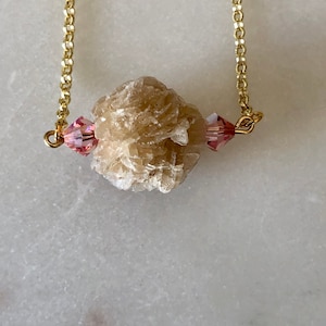 May include: A gold chain necklace with a light brown rose quartz crystal pendant and two pink crystal accents.