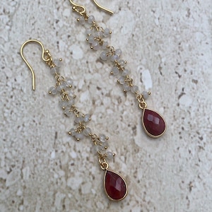 May include: Gold dangle earrings with a teardrop shaped red gemstone and a chain of small white beads.