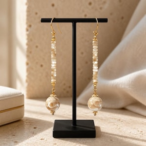 May include: A pair of long drop earrings featuring gold-tone hooks and hardware. Each earring consists of a vertical row of small, cylindrical, translucent beige beads topped with a larger, round, marbled beige and white bead at the base.