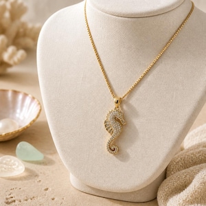 May include: A gold-toned necklace featuring a seahorse-shaped pendant encrusted with small, clear, sparkling stones. The pendant hangs from a delicate gold-toned box chain, creating a cohesive piece of jewelry with a polished, metallic finish.