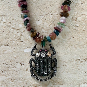 May include: A necklace made of multi-colored gemstone beads with a black and green jeweled beetle pendant.