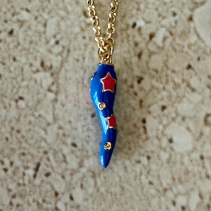 May include: A gold chain necklace with a blue enamel chili pepper pendant. The chili pepper has red stars on it.