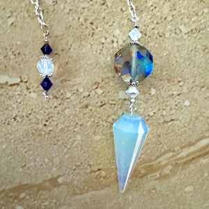 May include: Two crystal pendulums hanging from silver chains. One features a large, faceted, iridescent crystal with a blue hue, and a light blue, triangular crystal. The other has a series of blue and white beads.