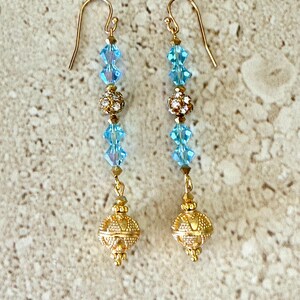 May include: Gold dangle earrings with blue crystal beads and gold ball accents.