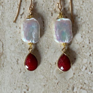 May include: Gold earrings with a white pearl and a red gemstone drop.