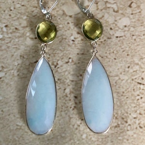 May include: A pair of silver dangle earrings with a teardrop-shaped white opal stone and a round green gemstone.