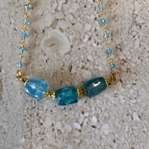 May include: A gold chain necklace with three light blue gemstone beads. The beads are rectangular in shape and have a slightly uneven surface.