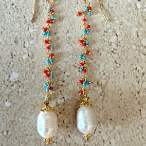 May include: A pair of long, dangling earrings with a white pearl at the bottom. The earrings are made of gold chain with small red and blue beads.