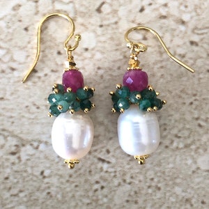 May include: A pair of gold earrings with a white pearl, green emerald, and pink ruby gemstone accents.