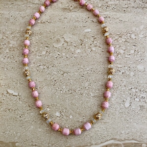 May include: A pink and gold beaded necklace with a toggle clasp. The beads are faceted and have a subtle shimmer.