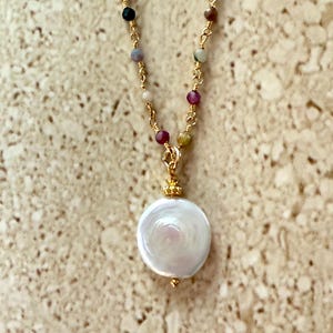May include: A gold chain necklace with a large white pearl pendant. The chain is adorned with small, colorful beads.