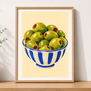 May include: A framed art print featuring a painting of a white bowl with thick vertical blue stripes filled with green olives. The olives are round with small red centres, set against a pale yellow background within a light wood frame.