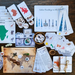 Op de afbeelding: Een set educatieve flashcards en activiteitenkaarten voor kinderen met een wereldkaart, continenten, dieren, gebouwen en een camera. De kaarten zijn gedrukt op wit karton met kleurrijke illustraties en tekst.