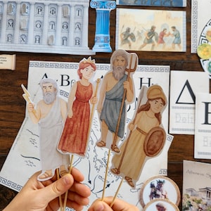 May include: A collection of educational materials featuring Greek mythology. Includes paper cutouts of Greek gods and goddesses on sticks, illustrations of Greek architecture, and educational cards with Greek letters and scenes.