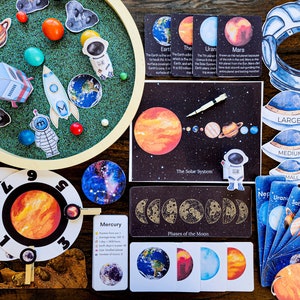 May include: A colourful set of educational materials for learning about the solar system. The set includes a felt board with planets, a rocket, and a moon, a solar system poster, a set of planet cards, a set of moon phase cards, and a set of planet size cards. The cards feature watercolour illustrations of the planets and moon.