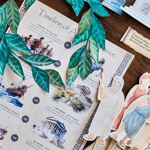 May include: A tabletop display featuring a timeline of ancient Greece, illustrated with images and text. Includes paper cutouts of figures, a decorative green leaf garland, and architectural elements. The text includes the words "Timeline of A" and "Greece".