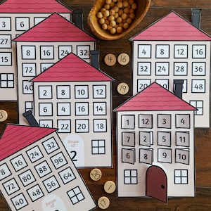 May include: Educational game featuring house-shaped cards with red roofs and numbered squares. Wooden tokens and a wooden bowl with small balls are also present. The cards are labeled "House of 2" and "House of 8", designed for learning math concepts.