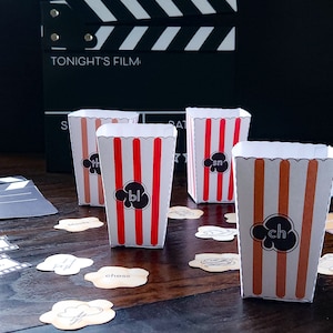 May include: Four popcorn boxes with red and brown stripes, each with a word bubble containing a two-letter blend. The boxes are on a wooden surface with word cards and a film clapperboard in the background. The clapperboard reads "TONIGHT'S FILM".