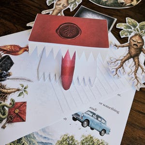 Puede incluir: Un libro desplegable de papel con una cubierta roja y un diseño de sello de cera, rodeado de varias ilustraciones impresas que incluyen una mandrágora, un coche azul, un paisaje y un collage circular de personajes en papel.