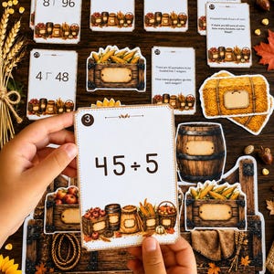 May include: A set of educational math flashcards featuring fall-themed illustrations of harvest baskets, pumpkins, and corn. Each card displays division problems or word problems with numbers and symbols. The cards have a white background with decorative borders and rustic autumn imagery at the bottom.