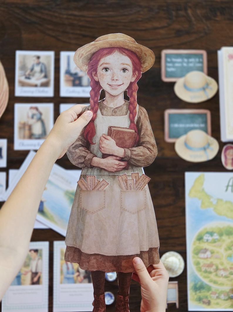 以下が含まれることがあります： 赤い三つ編みの女の子の紙の切り抜き。麦わら帽子とエプロンを着て、本を持っています。切り抜きは手で持たれており、背景には帽子や地図など、他の紙の切り抜きやイラストがあります。