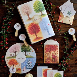 Könnte beinhalten: Eine Sammlung von saisonalen Schreibwaren und Dekorationsartikeln. Enthält ein Buch und Karten mit Illustrationen von Bäumen in verschiedenen Jahreszeiten, ein kreisförmiges Puzzle und dekorative Clips. Das Wort "Jahreszeiten" ist sichtbar.
