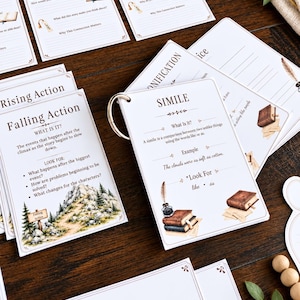 May include: A set of educational flashcards on a metal ring, featuring literary terms like Simile and Falling Action. Each white card includes printed definitions, examples, and illustrations of books, inkwells, and quills, with some cards laid out flat.