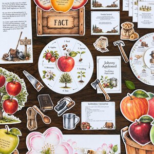 May include: A collection of educational paper cutouts featuring Johnny Appleseed themes, including a life cycle wheel, apple illustrations, a wooden crate, challenge cards, a vocabulary guide, and tools like a hammer, saw, and axe on a dark surface.